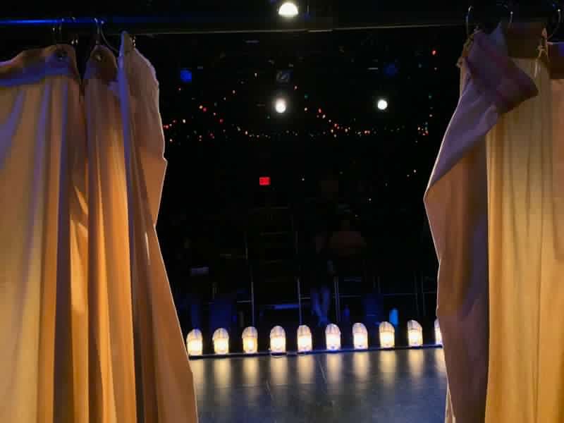 Looking into the audience from behind a partially opened curtain, the footlights aglow, you are onstage. 